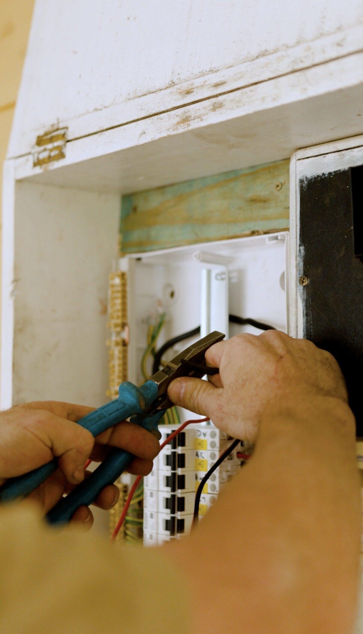 Close-up of an electrician’s hands wiring new circuit breakers into a switchboard